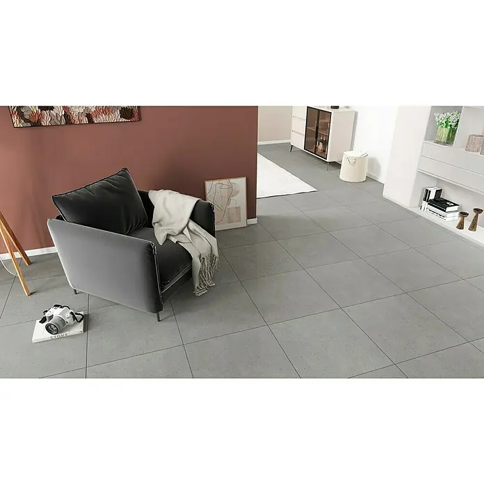 Feinsteinzeugfliese Serpico - 59,5 x 59,5 cm, Coolgrey, Glänzend - Einrichtungsszene mit modernem Sessel und dekorativen Elementen auf einem eleganten grauen Fliesenboden. Perfekt für Wohnraumgestaltung.