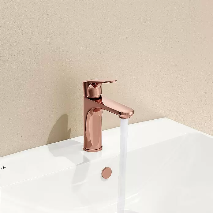 VitrA Waschtischarmatur Root Round - Kupfer - Roségoldene Armatur mit laufendem Wasser in einem weißen Waschbecken vor einer hellbeigen Wand.