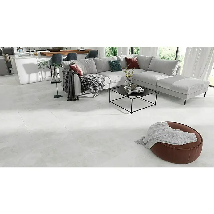 Feinsteinzeugfliese Geo White - 60 x 120 cm, Weiß, Schimmernd - Elegantes Wohnzimmer mit Fliesenboden in Weiß, Ecksofa, Couchtisch und Pouf. Die minimalistische Einrichtung erzeugt eine moderne Atmosphäre.