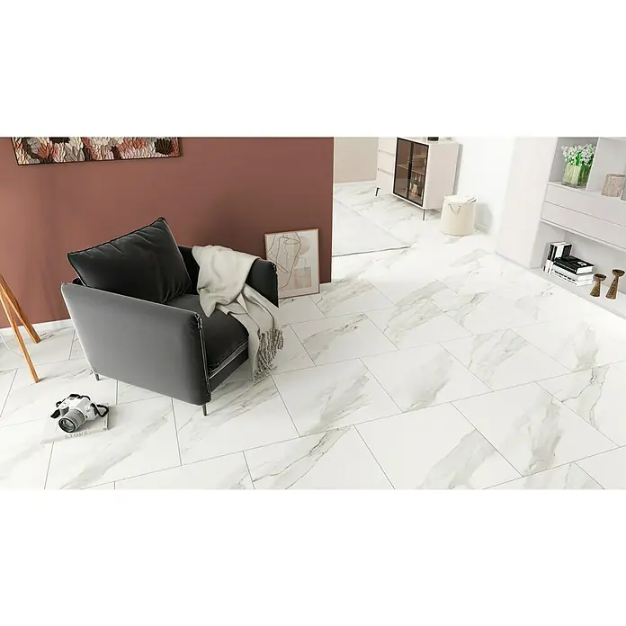 Feinsteinzeugfliese Torino Bianco - 60 x 60 cm, Weiß/Grau, Glänzend - Einladendes Wohnzimmer mit einem grauen Sessel, einer Kamera auf dem Boden und stilvollen weißen Fliesen, die für eine elegante Atmosphäre sorgen.