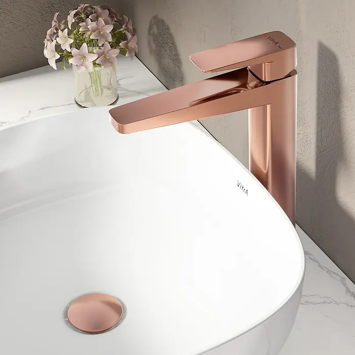 VitrA Waschtischarmatur Root Square - Höhe: 31 cm, Kupfer - Eine Nahaufnahme eines modernen, roségoldenen Wasserhahns der Marke VitrA auf einem weißen Waschbecken mit Marmorplatte und einem Blumengebinde.