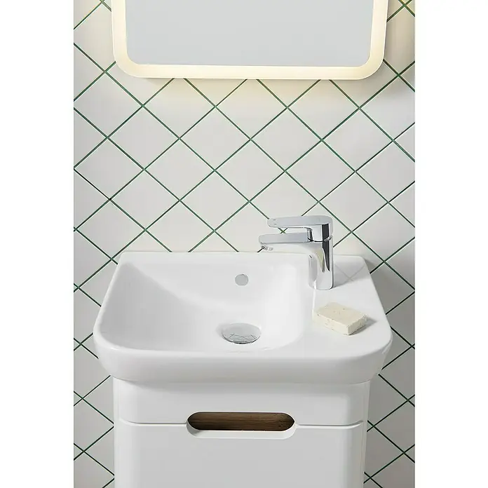 VitrA Sento Badmöbel-Set - Gesamtbreite Badmöbel: 50 cm, Weiß, Matt, DIN Anschlag: Rechts - Nahaufnahme eines modernen Waschbeckens mit Armatur, Seife und beleuchtetem Spiegel vor einem Hintergrund aus quadratischen Fliesen.