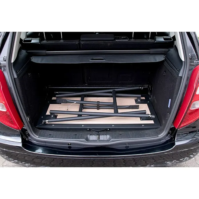 Rikta Werkbank klappbar - L x B: 100,5 x 50,6 cm, Arbeitshöhe: 84 cm, Belastbarkeit: 150 kg, Schwarz, Holz - Zusammengeklappter Tisch im Kofferraum eines schwarzen Autos. Der Tisch hat ein helles Holzdesign und ein schwarzes Gestell.