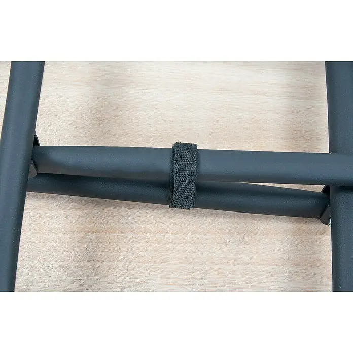 Rikta Werkbank klappbar - L x B: 100,5 x 50,6 cm, Arbeitshöhe: 84 cm, Belastbarkeit: 150 kg, Schwarz, Holz - Nahaufnahme des Klettverschlusses, der zwei schwarze Metallstangen auf einem hellbraunen Holzboden zusammenhält. Praktische Lösung zur Fixierung.