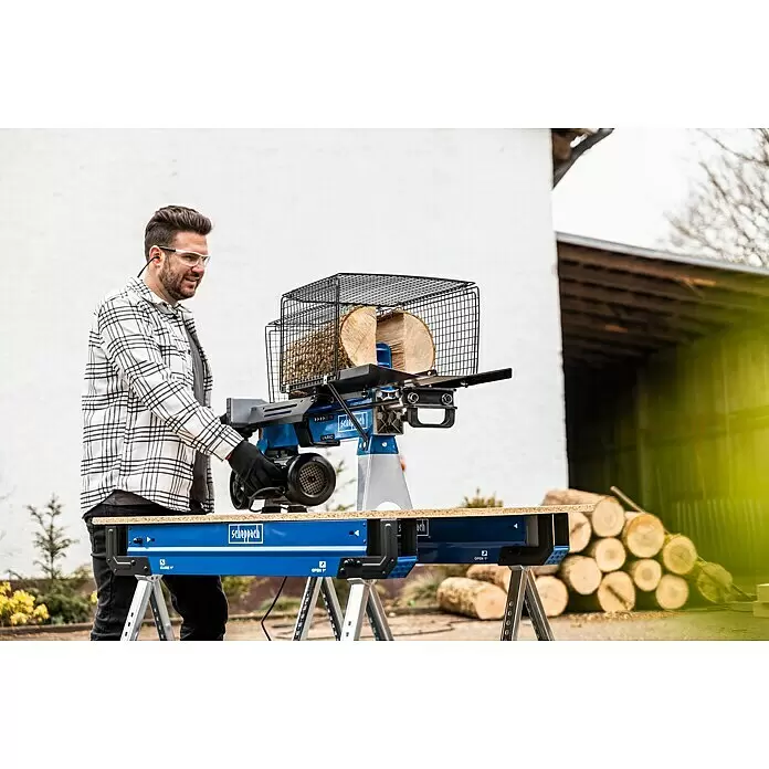 Scheppach Holzspalter LS700UG mit Untergestell - 7 t, Max. Spaltgutlänge: 52 cm - 200 mm - Ein Mann in Schutzkleidung bedient einen blau-silbernen Scheppach Holzspalter, der Holzscheite auf einer Werkbank spaltet.
