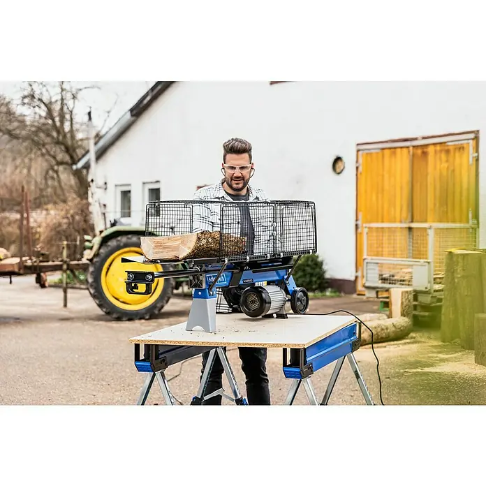 Scheppach Holzspalter LS700UG mit Untergestell - 7 t, Max. Spaltgutlänge: 52 cm - 200 mm - Holzspalter von Scheppach mit Schutzgitter und stehendem Holz auf einer Werkbank für die Holzbearbeitung im Außenbereich.