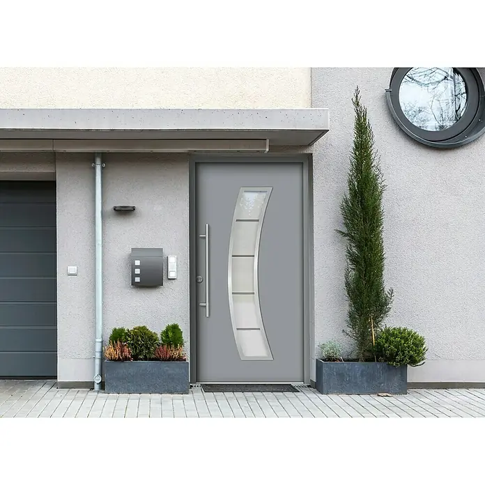 Splendoor Haustür Thermodoor PLUS SP10 - 110 x 210 cm, DIN Anschlag: Links, Verkehrsgrau - Eine moderne Haustür in Grau mit einem vertikalen, gebogenen Glaseinsatz, eingebettet in eine stilvolle Fassade mit Pflanzen.