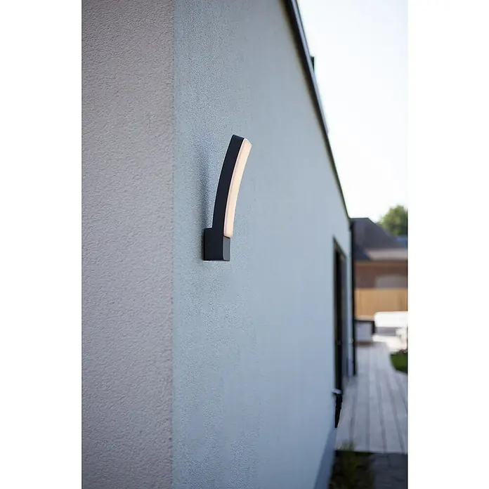 Lutec Aplique exterior LED Kira - 17,3 W, 8,3 x 11 x 31,1 cm, Antracita, IP54 - Primer plano de una lámpara de pared exterior curvada moderna con iluminación LED, montada en una pared texturizada.