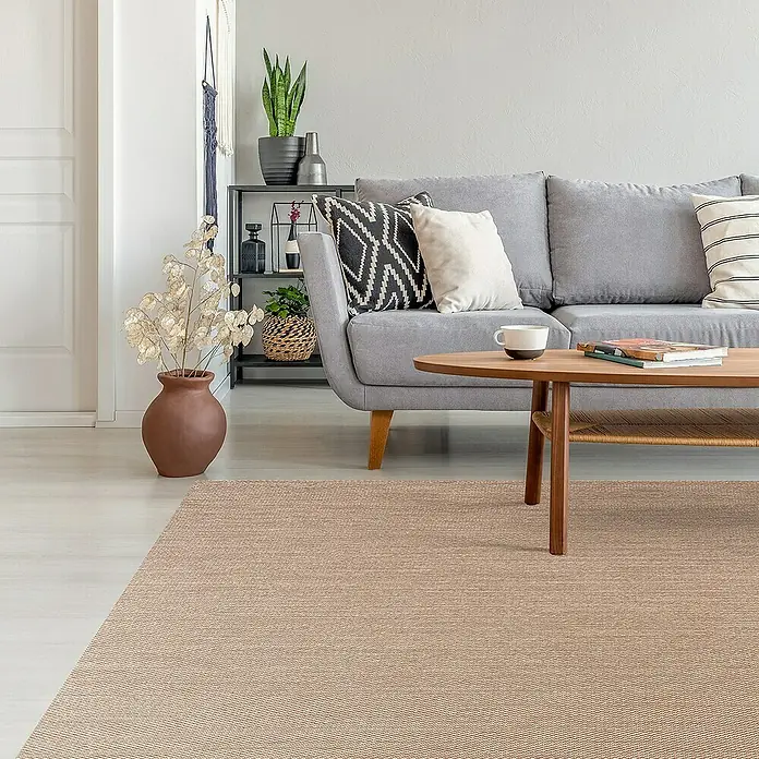 Alfombra de vinilo Living Lisa - Sisal, 180 x 120 cm - Salón con una alfombra beige, un sofá gris, una mesa de madera y una planta.