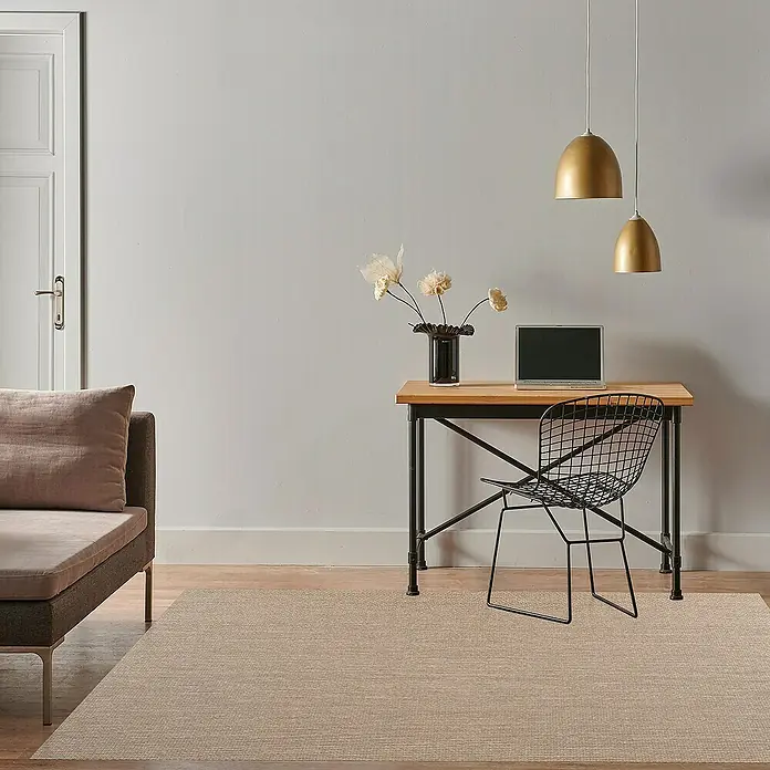 Alfombra de vinilo Living Lisa - Sisal, 180 x 120 cm - Una alfombra clara está colocada debajo de un escritorio con una silla, complementada con un sofá y lámparas colgantes doradas.