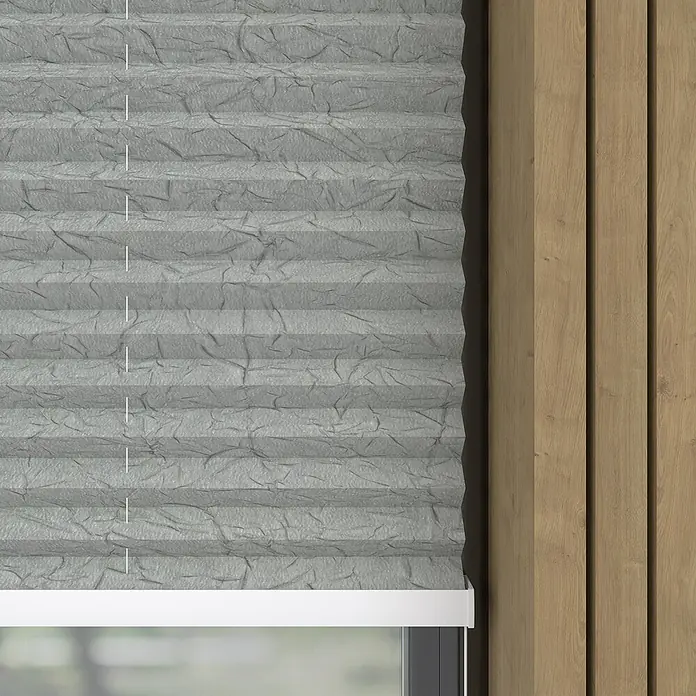 Expo Ambiente PlisseeB x H: 110 x 130 cm, Hellgrau - Nahaufnahme einer grauen, gefalteten Fensterjalousie mit unregelmäßiger Textur, montiert neben einer Holzvertäfelung.