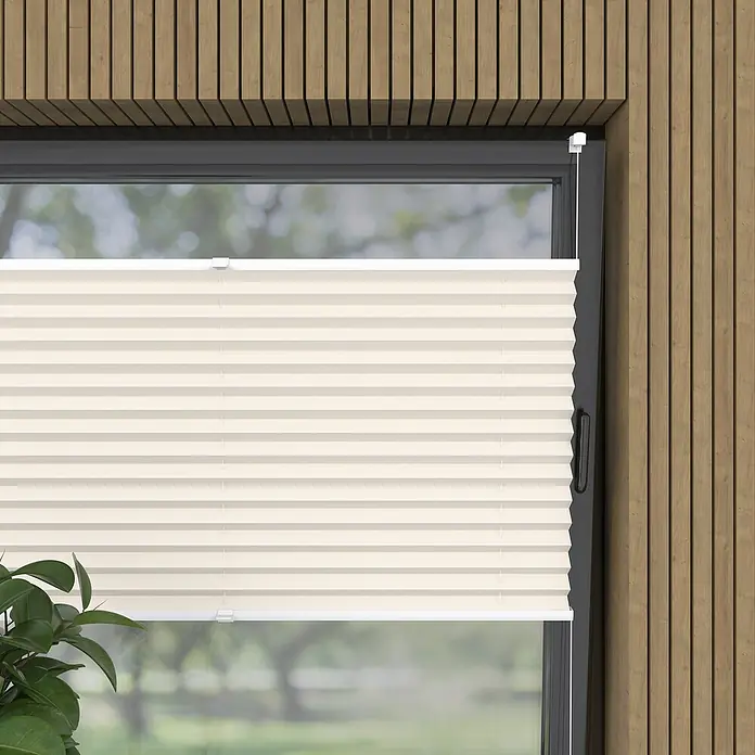 Plissee Basic VS Thermo - B x H: 45 x 130 cm, Altweiß, Verdunkelnd - Nahaufnahme einer beigen Plissee-Jalousie vor einem Fenster mit Holzrahmen, die Privatsphäre und Lichtschutz bietet.