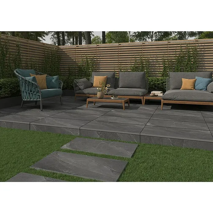 Terrassenfliese Monte 2.0 - 39,7 x 79,7 x 2 cm, Anthrazit, Matt - Das Bild zeigt einen Außenbereich mit anthrazitfarbenen Terrassenplatten, Gartenmöbeln und einem modernen Holzzaun.