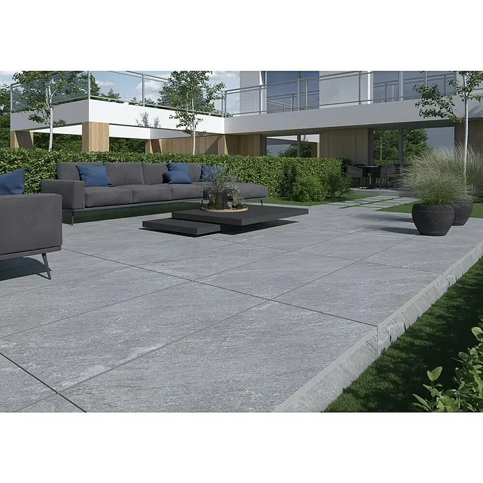 Terrassenfliese Piazza 2.0 - 59,7 x 119,7 x 2 cm, Grau, Matt - Moderne Terrasse mit grauen Fliesen, stilvollem Sofa, Couchtisch und Pflanzenkübeln.