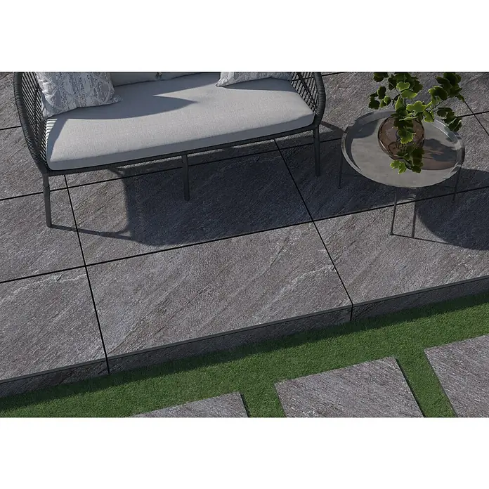 Terrassenfliese Piazza 2.0 - 59,7 x 119,7 x 2 cm, Anthrazit, Matt - Das Bild zeigt stilvolle graue Steinplatten, die einen modernen Außenbereich gestalten, ergänzt durch eine Sitzgruppe und Beistelltisch.