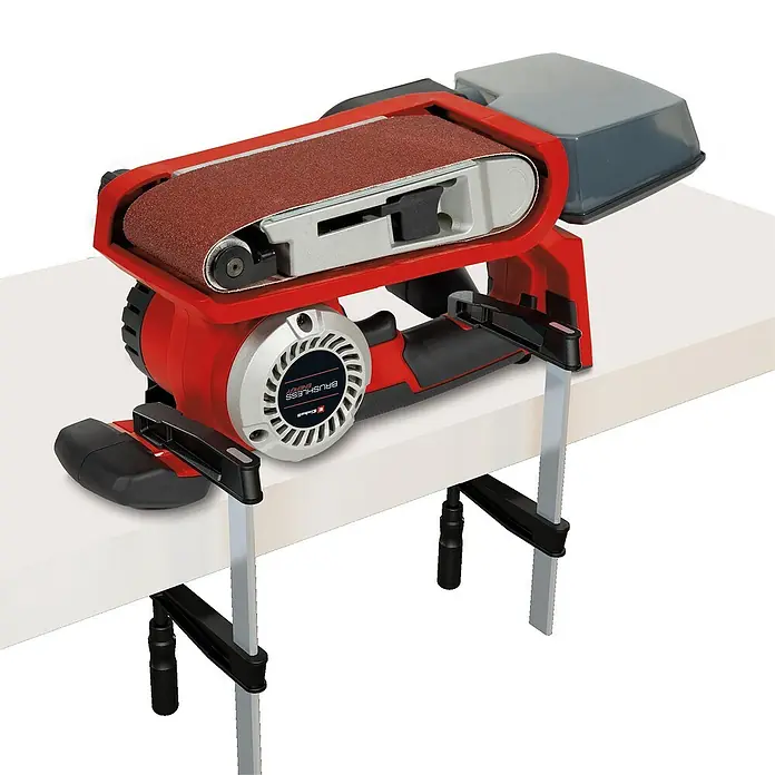 Einhell Professional PXC 18V Lijadora de banda de batería TP-BS 18/457 Li BL - Solo - 18 V, Sin batería, Velocidad de cinta: 120 m/min - 250 m/min - Aquí hay una lijadora de banda de mesa Einhell TE-BS 75 en rojo y plata, fijada a un banco de trabajo blanco.