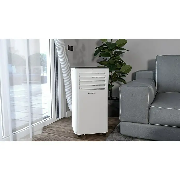 Proklima Mobiles Klimagerät WiFi - 2.000 W, Raumgröße: 20 m², Weiß/Schwarz - Ein tragbares Klimagerät steht neben einem Fenster und einem Sofa und sorgt für eine angenehme Temperatur.