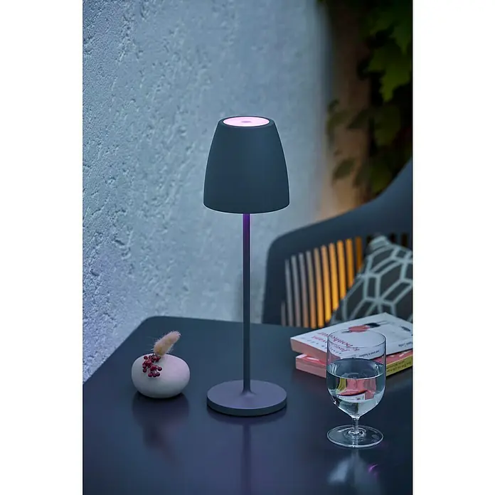 Lavida Akku-Tischleuchte Silea - 3,3 W, Anthrazit, Lichtfarbe: RGBW - Eine moderne Tischlampe mit sanftem, farbigem Licht, die eine gemütliche Atmosphäre auf einem Tisch mit Dekoration und Getränken schafft.