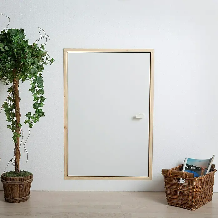Sogem Compuerta Easy Access - An x Al: 70 x 80 mm - Una puerta blanca sencilla con marco de madera clara empotrada en una pared blanca, complementada con una planta en maceta y una cesta con revistas.