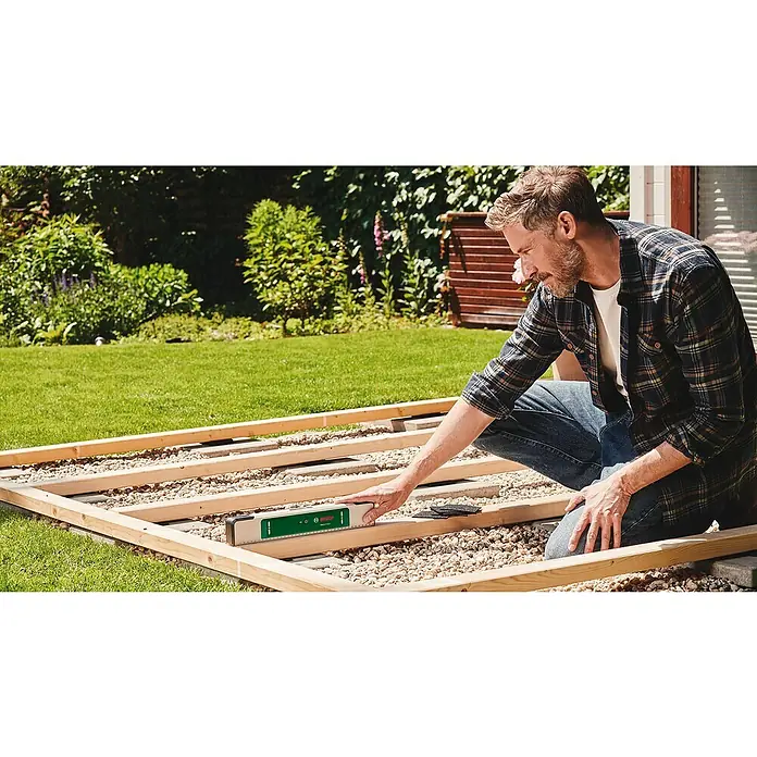 Bosch Easy Wasserwaage EasySpiritLevel - L x B x H: 40 x 3,2 x 6,4 cm, Kunststoff, Grün, Silber - Ein Mann benutzt eine Bosch Wasserwaage, um eine Holzkonstruktion im Garten auszurichten, was die Präzision des Werkzeugs hervorhebt.