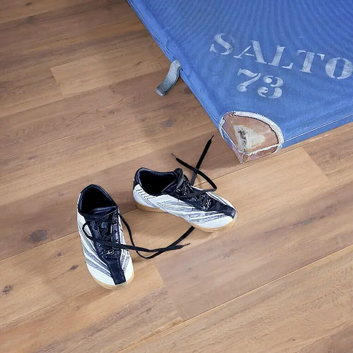 Parkettmuster Eiche Lindau - 280 x 160 x 15 mm, Landhausdiele - Ein Paar Sportschuhe mit schwarzen Schnürsenkeln liegen neben einer blauen Matte mit der Aufschrift "SALTO 73" auf einem Holzboden.
