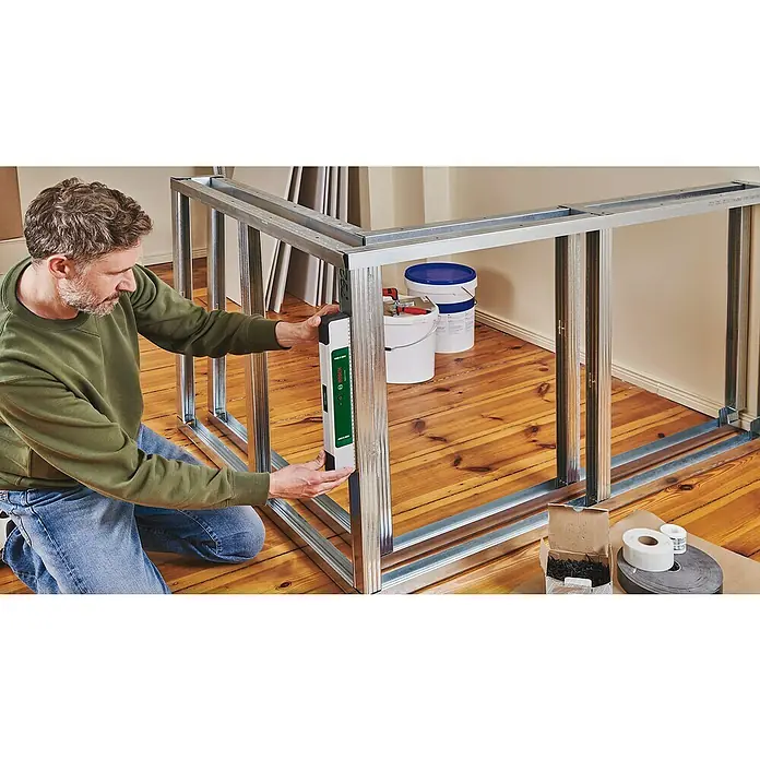 Bosch Easy Wasserwaage EasySpiritLevel - L x B x H: 40 x 3,2 x 6,4 cm, Kunststoff, Grün, Silber - Ein Mann überprüft mit einem Bosch-Laser die Ausrichtung eines Metallrahmens auf einem Holzboden, während er eine neue Struktur baut.