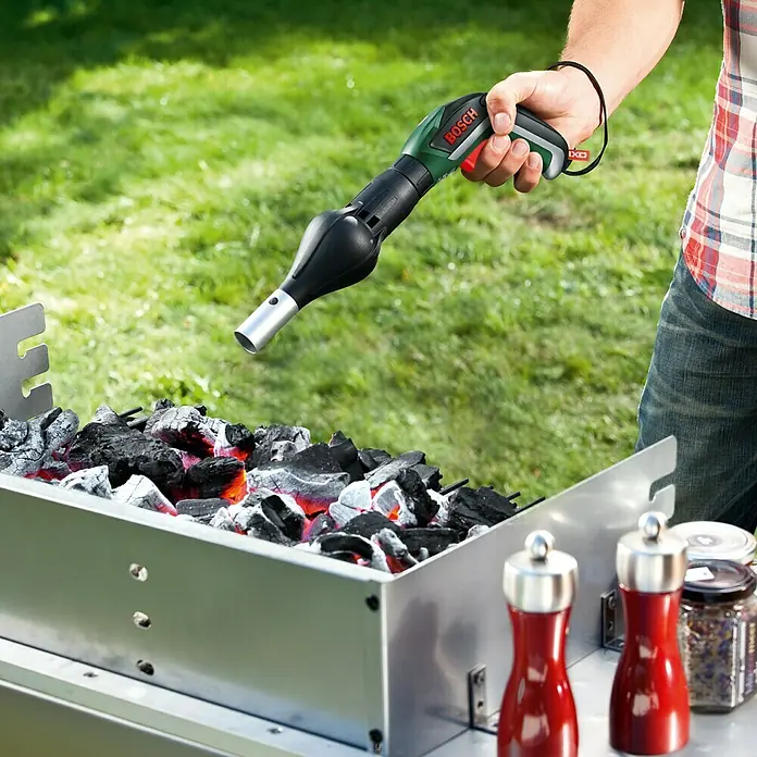 Bosch Gebläseaufsatz - Passend für: Bosch Easy Akkuschrauber IXO III/IV/V/VI - Ein Mann hält einen Bosch Anzünder über einen Grill. Der Anzünder ist schwarz und grün und hat einen silbernen Aufsatz.