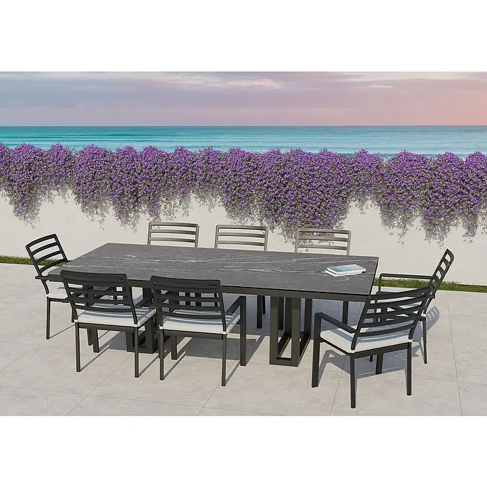 Mesa de jardín Doble Bridge - L x An x Al: 260 x 120 x 74 cm, Aluminio/Cerámica, Cardoso Gray - Un moderno juego de comedor con una mesa gris y sillas negras con cojines blancos al aire libre con vistas al mar.