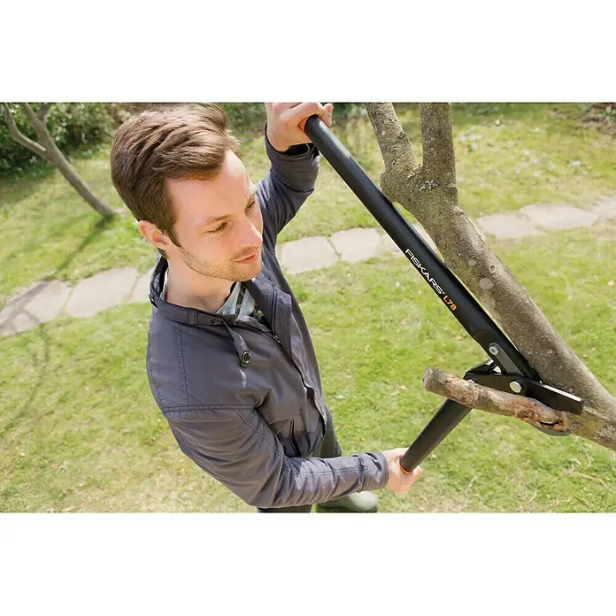 Fiskars Hand-Astschere PowerGear II L78 - Länge: 69,2 cm, Max. Aststärke: 50 mm, Stahl, Orange/Schwarz - Ein Mann benutzt eine Fiskars L78 Astschere, um einen Ast zu schneiden. Das Werkzeug ist schwarz mit orangefarbenen Akzenten.