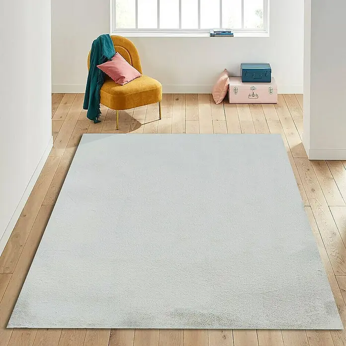 Alfombra de pelo corto Tiana - Crudo, 110 x 60 cm - Una alfombra grande, rectangular y esponjosa en una habitación luminosa con suelos de madera.