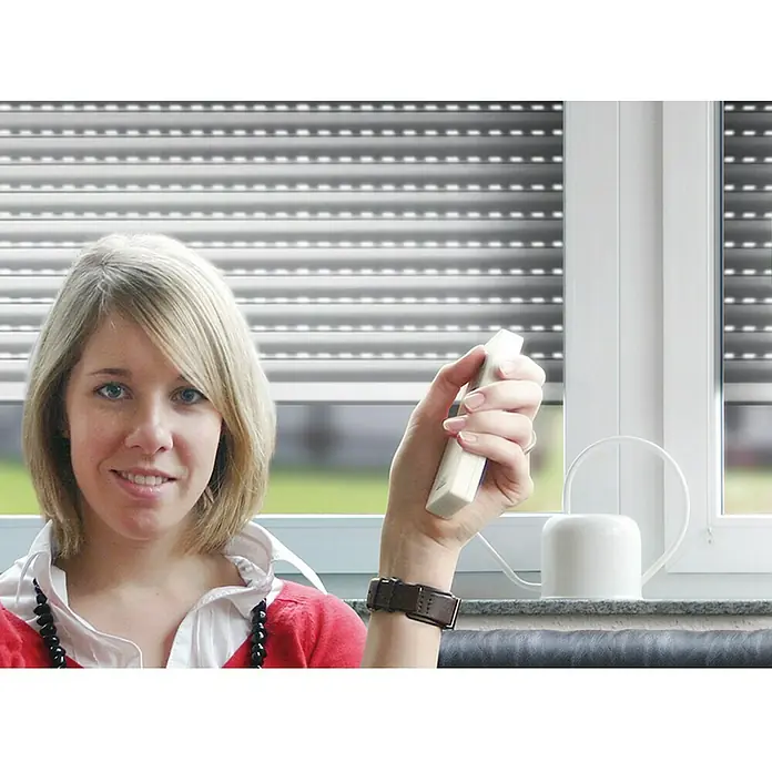 Schellenberg Control remoto con 1 canal - Blanco, Específico para: Enrollador de cable para persianas Schellenberg - Mujer utilizando un mando a distancia para persianas enrollables. Las persianas están cerradas, proporcionando privacidad y protección.