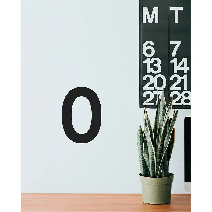 Vinilo de pared Número 0 - 4 x 9 cm, Negro, Plástico - Planta de interior en una maceta verde oliva frente a una pared con un cero negro y un calendario.