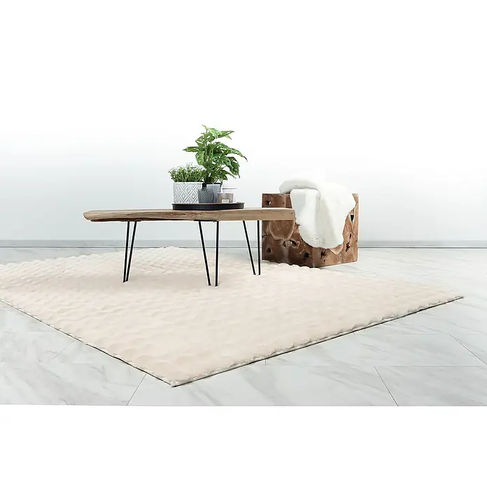 Hochflorteppich Harmony - Ivory, 170 x 120 cm, 100 % Polyester (Flor) - Der Fokus liegt auf dem beigen Teppich mit geometrischem Muster, der unter einem Holztisch und einem Hocker mit einem weißen Fell liegt.