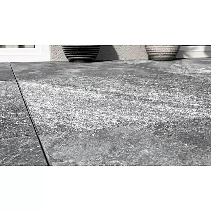 Terrassenfliese Cera 2.0 - 80 x 80 x 2 cm, Quarz Nero, Matt - Graue, strukturierte Terrassenfliesen als Außenboden, mit dekorativen Töpfen im unscharfen Hintergrund.