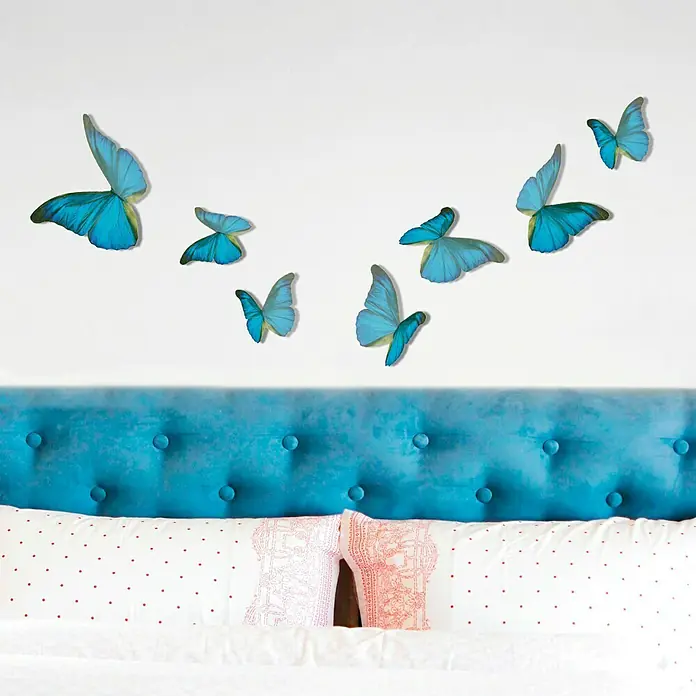 Vinilo de pared 3D Mariposa - 14 x 11 cm, Azul/Negro, Plástico - Decoración de pared: Mariposas azules adornan una pared sobre un cabecero y almohadas de terciopelo azul, creando un ambiente sereno en el dormitorio.