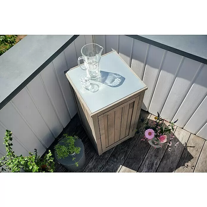 Butenkist Geräteschrank NEELE - 45 x 45 x 85 cm, Warm Grey - Hölzerner Outdoor-Aufbewahrungsschrank mit hellgrauer Platte, als Beistelltisch auf einer Terrasse mit Getränken und Blumen genutzt.