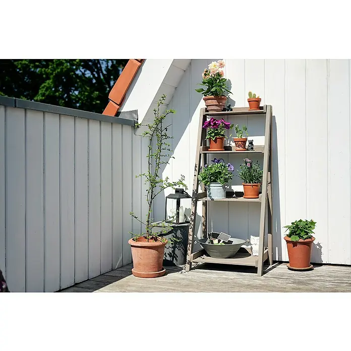 Butenkist Blumentreppe GESA - 40 x 48 x 105 cm, Nadelholz, Warm Grey - Ein dreistufiges Pflanzenregal aus Holz mit Topfpflanzen auf einer Terrasse vor einer weißen Wand.