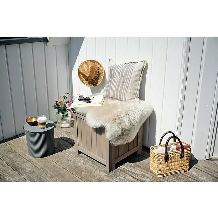 Butenkist Garten-Aufbewahrungsbox HILLE - Warm Grey, Holz - Ein stilvolles Outdoor-Arrangement mit einer Holzaufbewahrungsbox, die als Sitzgelegenheit dient, ergänzt durch ein Kissen, Fell und Accessoires.