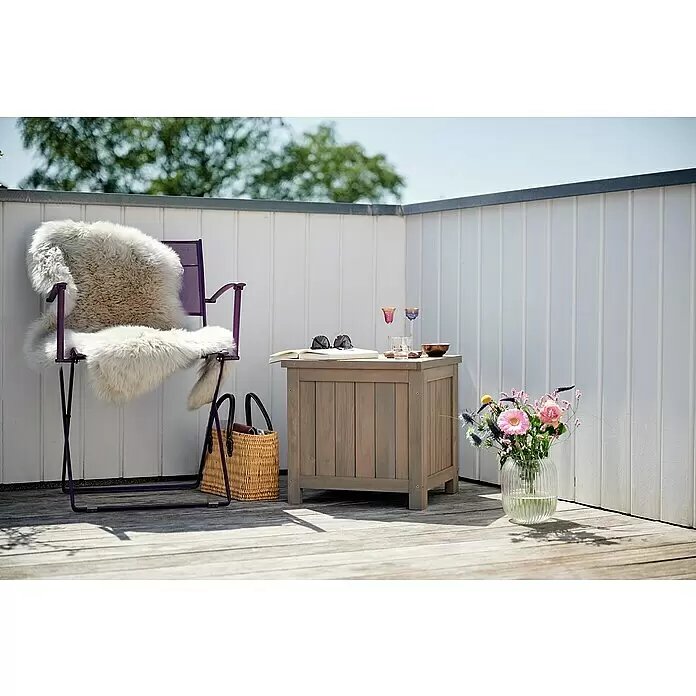 Butenkist Garten-Aufbewahrungsbox HILLE - Warm Grey, Holz - Graue Holz-Aufbewahrungsbox auf der Terrasse, als Beistelltisch mit Buch und Getränken neben einem lila Stuhl.