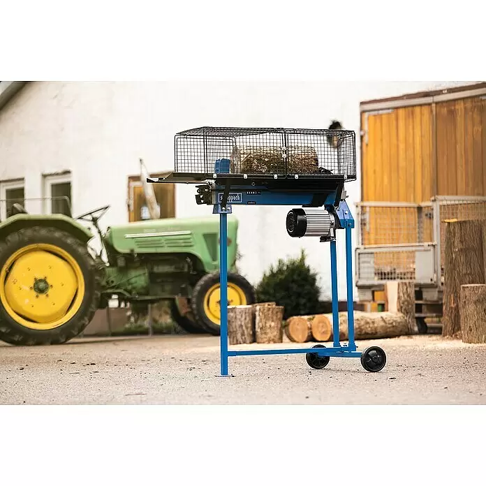 Scheppach Holzspalter LS700UG mit Untergestell - 7 t, Max. Spaltgutlänge: 52 cm - 200 mm - Blau-schwarzer Metall-Sägebock für Holzstämme mit Motor und Rädern, im Freien nahe einem grünen Traktor.