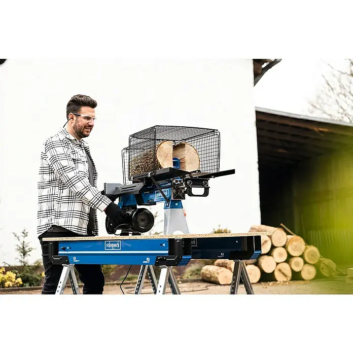 Scheppach Holzspalter LS700UG mit Untergestell - 7 t, Max. Spaltgutlänge: 52 cm - 200 mm - Ein Mann bedient einen Scheppach Holzspalter mit Sicherheitskäfig. Der Holzspalter steht auf einem blauen Arbeitstisch, im Hintergrund Holzstapel.