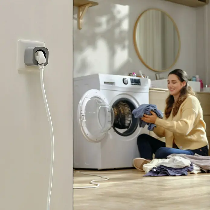 EcoFlow Steckdose Smart Plug - Grau - Eine Steckdose mit einem grauen Adapter und einem weißen Kabel, das zu einer Waschmaschine führt, neben einer Frau, die Wäsche sortiert.