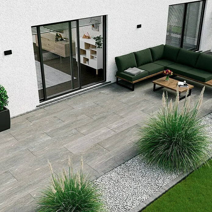 Esterno 20 T by Palazzo Terrassenfliese Davos - 40 x 120 x 2 cm, Greige, Matt - Bild einer modernen Terrasse mit grauen Terrassenplatten, einer grünen Sofaecke und dekorativem Ziergras.