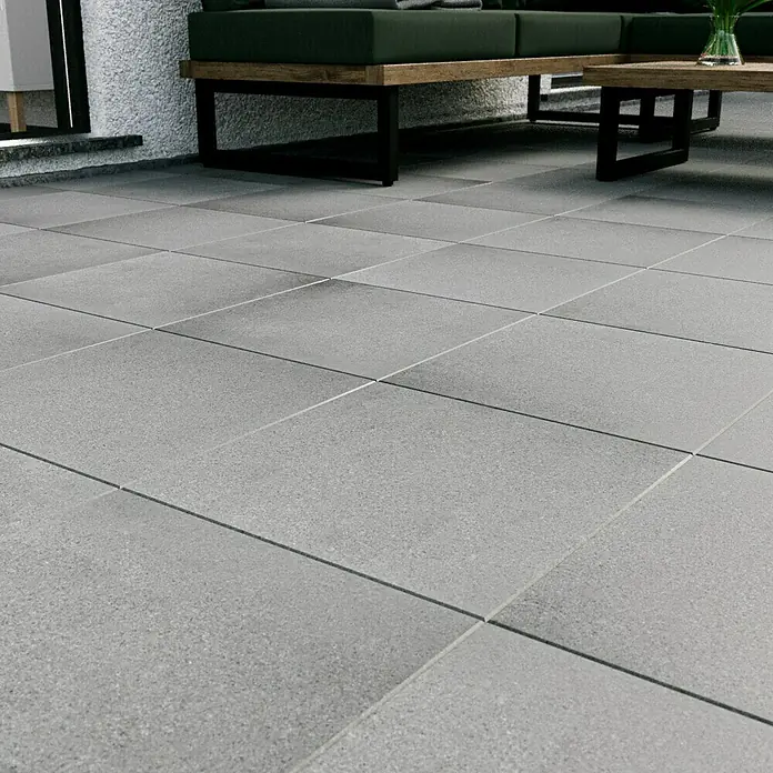 Terrassenplatte Titanio Glatt - 40 x 40 x 4 cm, Grau, Beton - Das Bild zeigt einen Terrassenbereich mit quadratischen, grauen Steinplatten, die ein modernes und schlichtes Design aufweisen. Ideal für Außenbereiche.