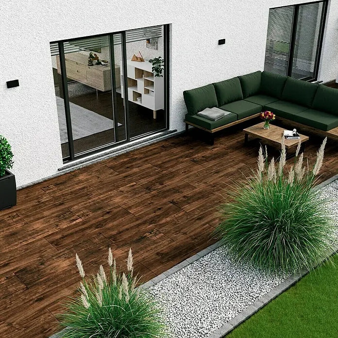 Esterno 20 T by Palazzo Terrassenfliese Harmonie - 40 x 120 x 2 cm, Zeder, Matt - Blick auf eine Terrasse mit Holzboden, einer grünen Lounge-Garnitur und dekorativen Gräsern, die eine warme und einladende Atmosphäre schafft.
