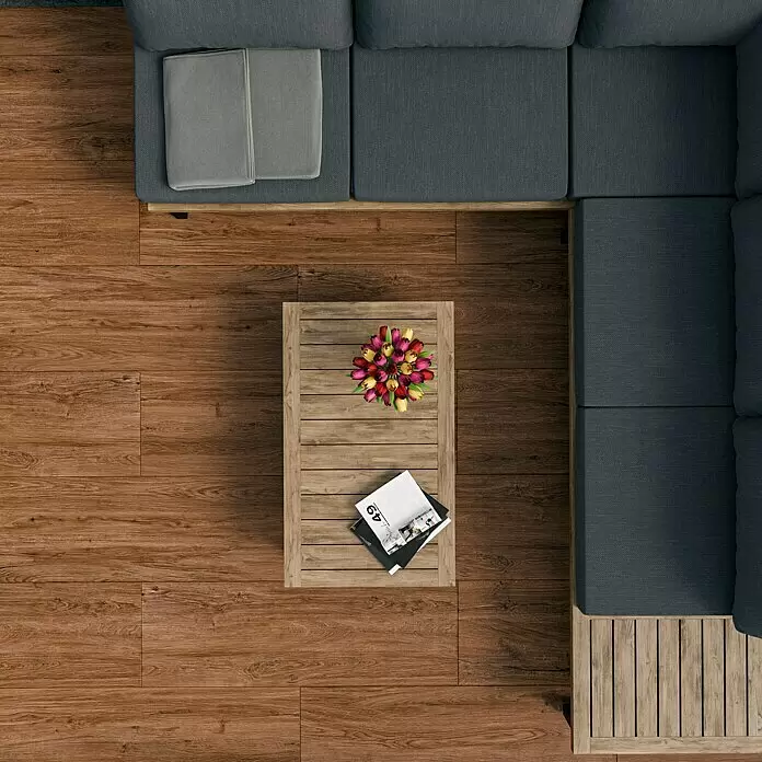Marazzi Terrassenfliese Esterno 20T Woodliving Scuro - 40 x 120 x 2 cm, Braun, Matt - Blick von oben auf ein L-förmiges Outdoor-Sofa mit grauen Kissen und Holzrahmen, dazu ein passender Holztisch mit Blumendeko.
