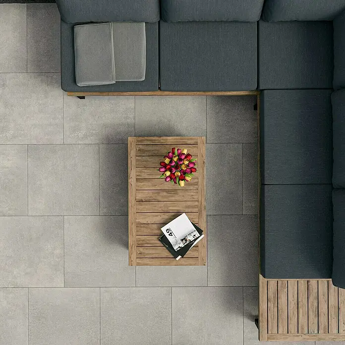 Marazzi Terrassenfliese Esterno 20T Plaster Grey - 60 x 60 x 2 cm, Grau, Matt - Draufsicht auf ein modernes Outdoor-Lounge-Set mit Couch, Holztisch mit Blumen und Zeitschriften auf einer Terrasse.