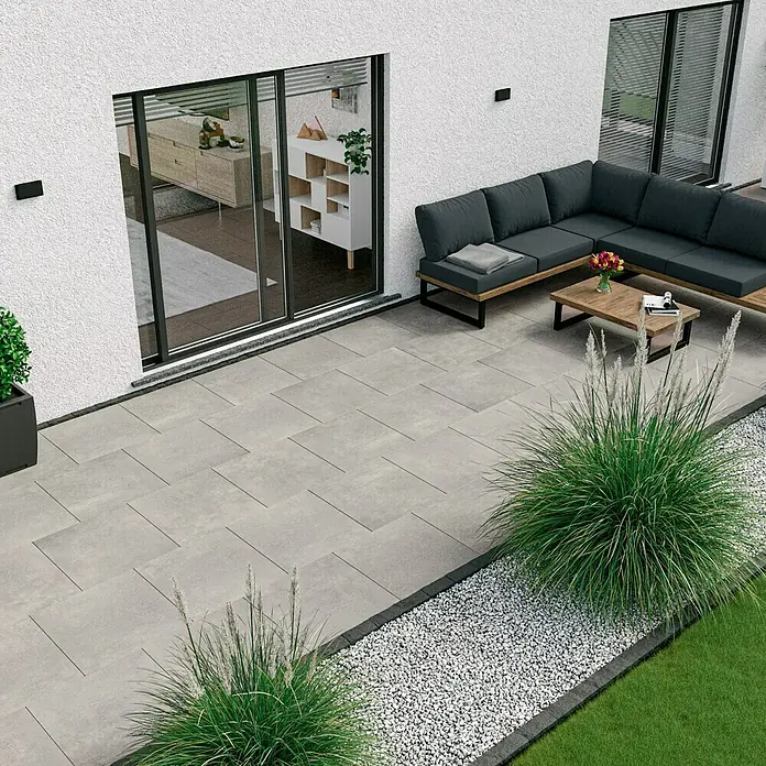 Marazzi Terrassenfliese Esterno 20T Plaster Grey - 60 x 60 x 2 cm, Grau, Matt - Das Bild zeigt eine moderne Terrasse mit grauen Pflastersteinen, einer grauen Couchgarnitur und dekorativem Kiesbereich.
