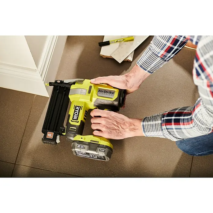 Ryobi ONE+ Akku-Nagler R18GN18-0 - 18 V, Ohne Akku, Länge Nagel: 15 mm - 50 mm - Nahaufnahme eines Ryobi AirStrike Akku-Nagelgeräts, das auf Fliesenboden platziert ist und von einer Person gehalten wird.