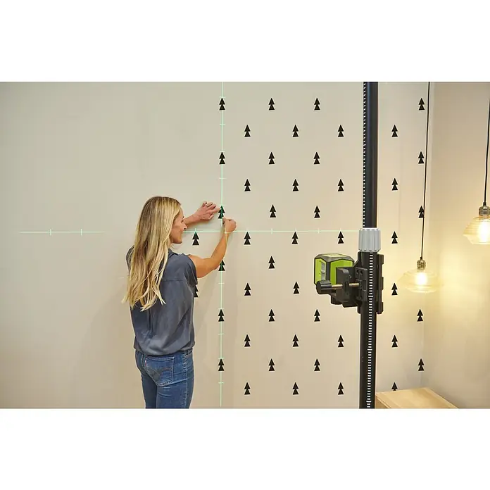 Ryobi Kreuzlinienlaser RBCLLG2 mit Skalamarkierung - Max. Arbeitsbereich: 15 m - Frau verwendet einen Rotationslaser zur präzisen Ausrichtung von Deko-Aufklebern auf einer Wand. Das Werkzeug projiziert sichtbare grüne Linien für Genauigkeit.